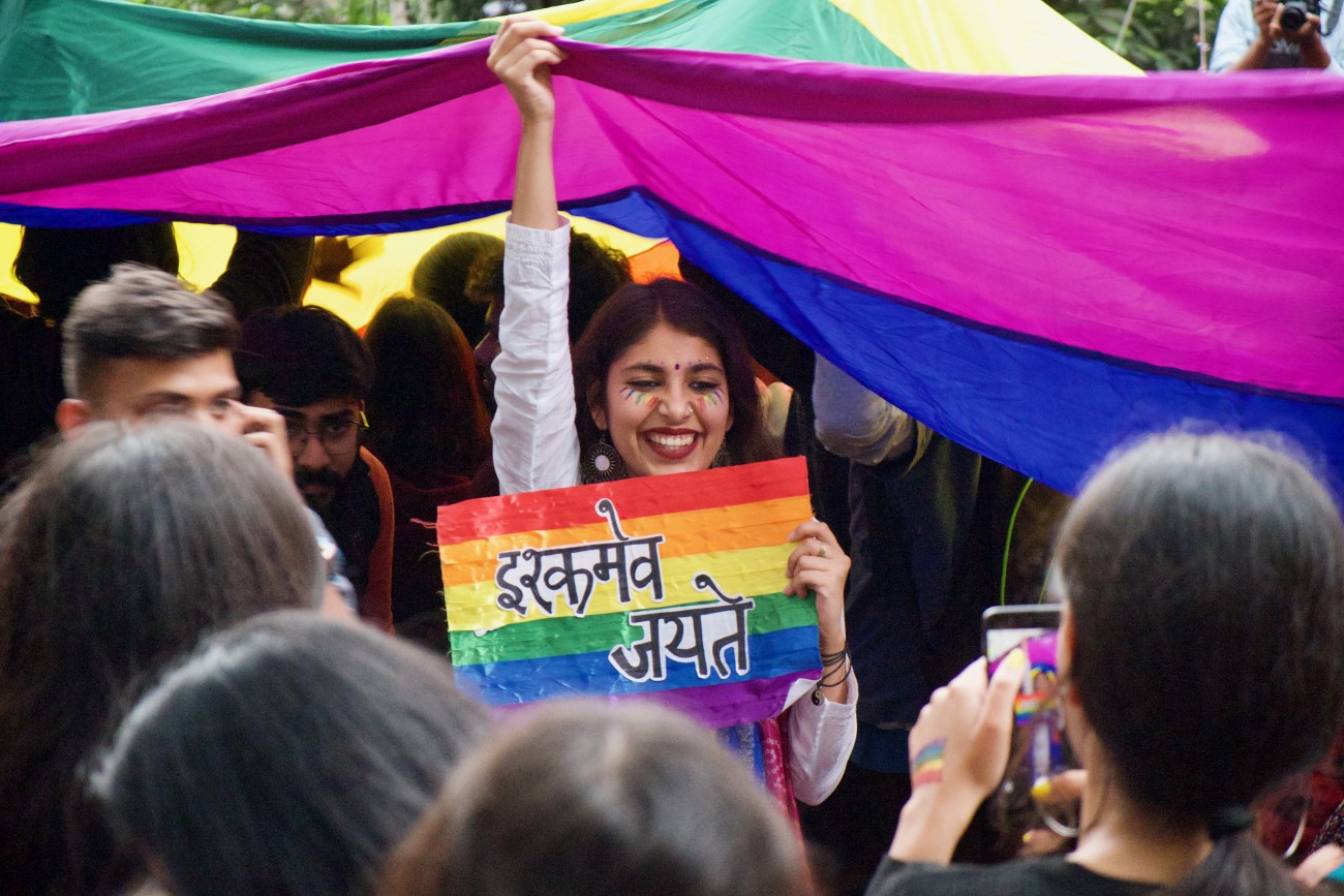 Woman holding a rainbow sign, underneath a huge rainbow flag
