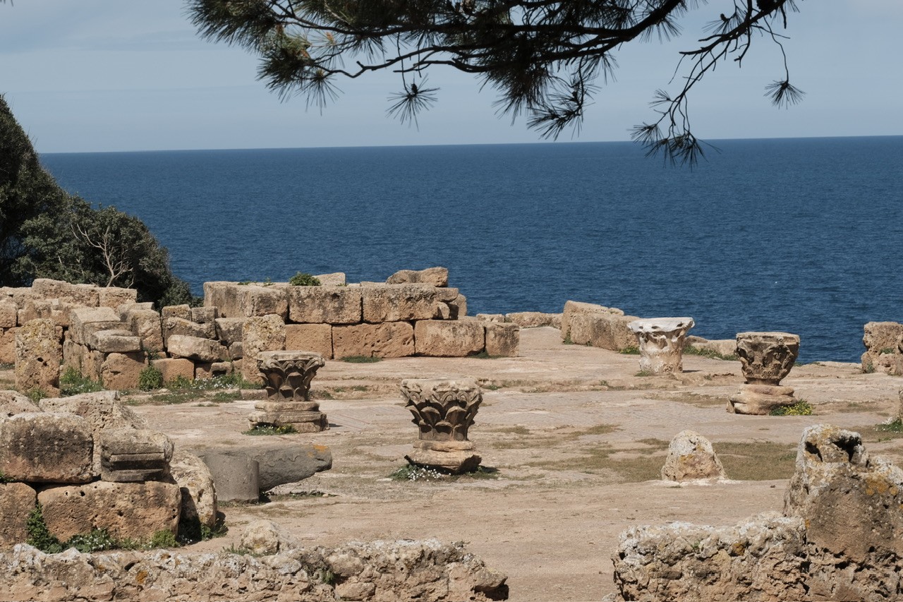Some Roman ruins with a couple of pieces of column and a mosaic floor with the sea in the background